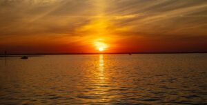 barnegat-bay-sunset-lbi-tourism Sun setting over Barnegat Bay with a boat on the water, Long Beach Island, New Jersey